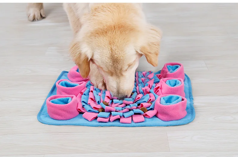 Un perro con la nariz metida en un juguete que parece estar diseñado para mantener a los perros entretenidos y estimulados mentalmente. El juguete tiene una base azul con tela rosa y azul cortada en forma de espiral, que se asemeja a una cuerda retorcida o un diseño trenzado.