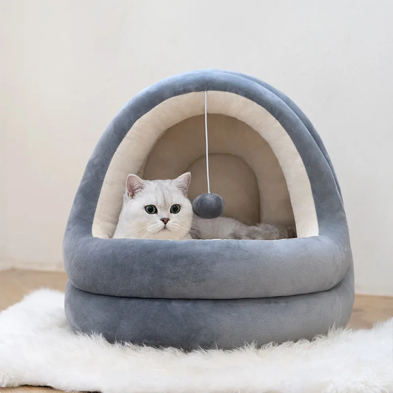 Un gato blanco sentado dentro de una cama para gatos. La cama tiene un diseño curvo con una combinación de colores gris y blanco, y hay un pequeño juguete colgando de la parte superior, que parece ser una pelota.