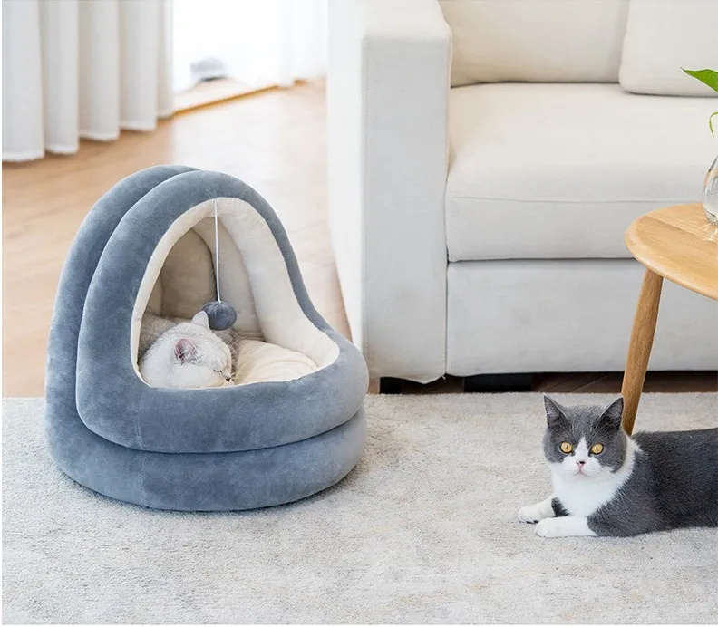 Un ambiente interior acogedor con dos gatos. A la izquierda, hay una cama para gatos con un gato blanco y gris durmiendo dentro. La cama tiene un diseño curvo y parece suave y cómoda.