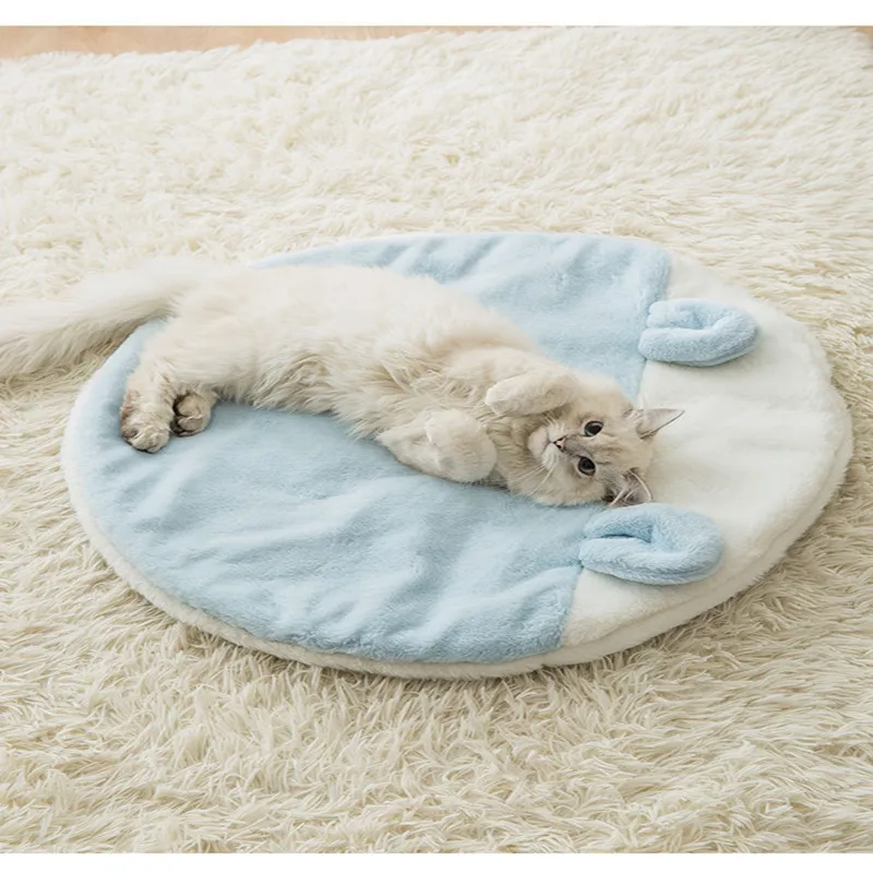 Un gato blanco acostado boca arriba sobre una cama redonda y azul para mascotas. El gato parece relajado y cómodo, con las patas en el aire. La cama está colocada sobre una alfombra peluda blanca, lo que contribuye a la atmósfera acogedora y suave de la escena.