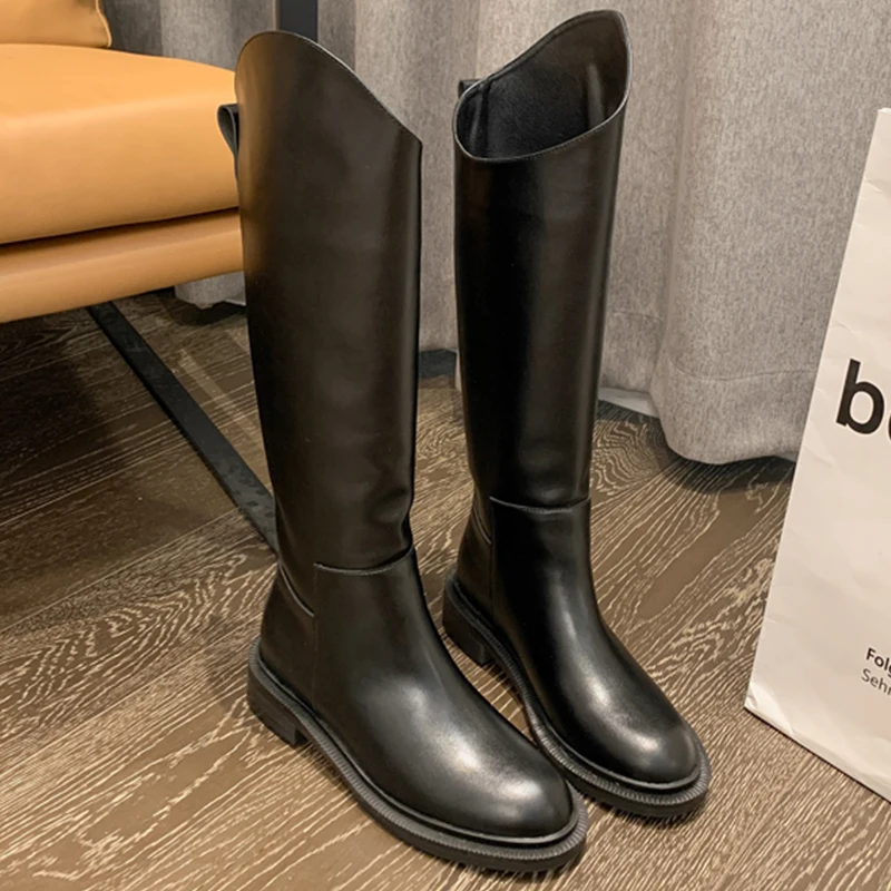 Un par de botas negras están parados en un piso de madera.