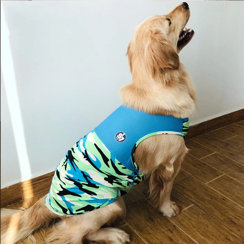 Un perro que lleva un chaleco con estampado de camuflaje azul y verde. El perro parece ser un Golden Retriever y está sentado en un suelo de madera con la boca abierta, posiblemente ladrando o bostezando.
