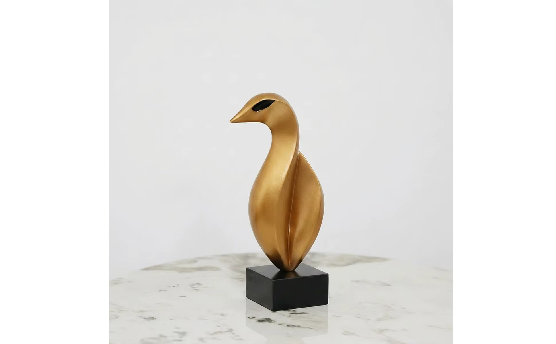 Escultura de pájaro dorada con cuello curvado sobre base negra